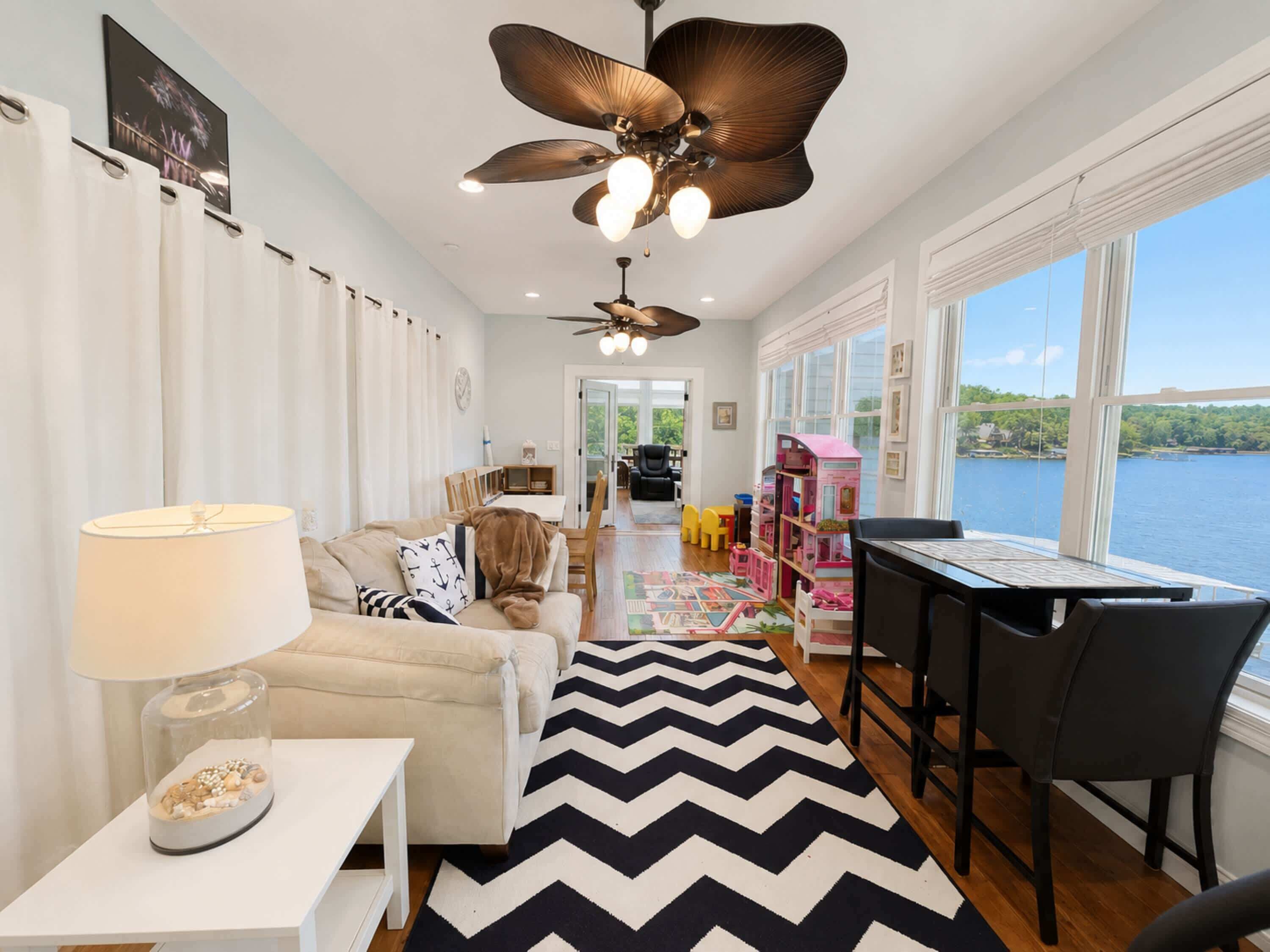 Un salon comprenant un canapé, une table avec une lampe, un ventilateur de plafond, un tapis et une vue sur un lac.