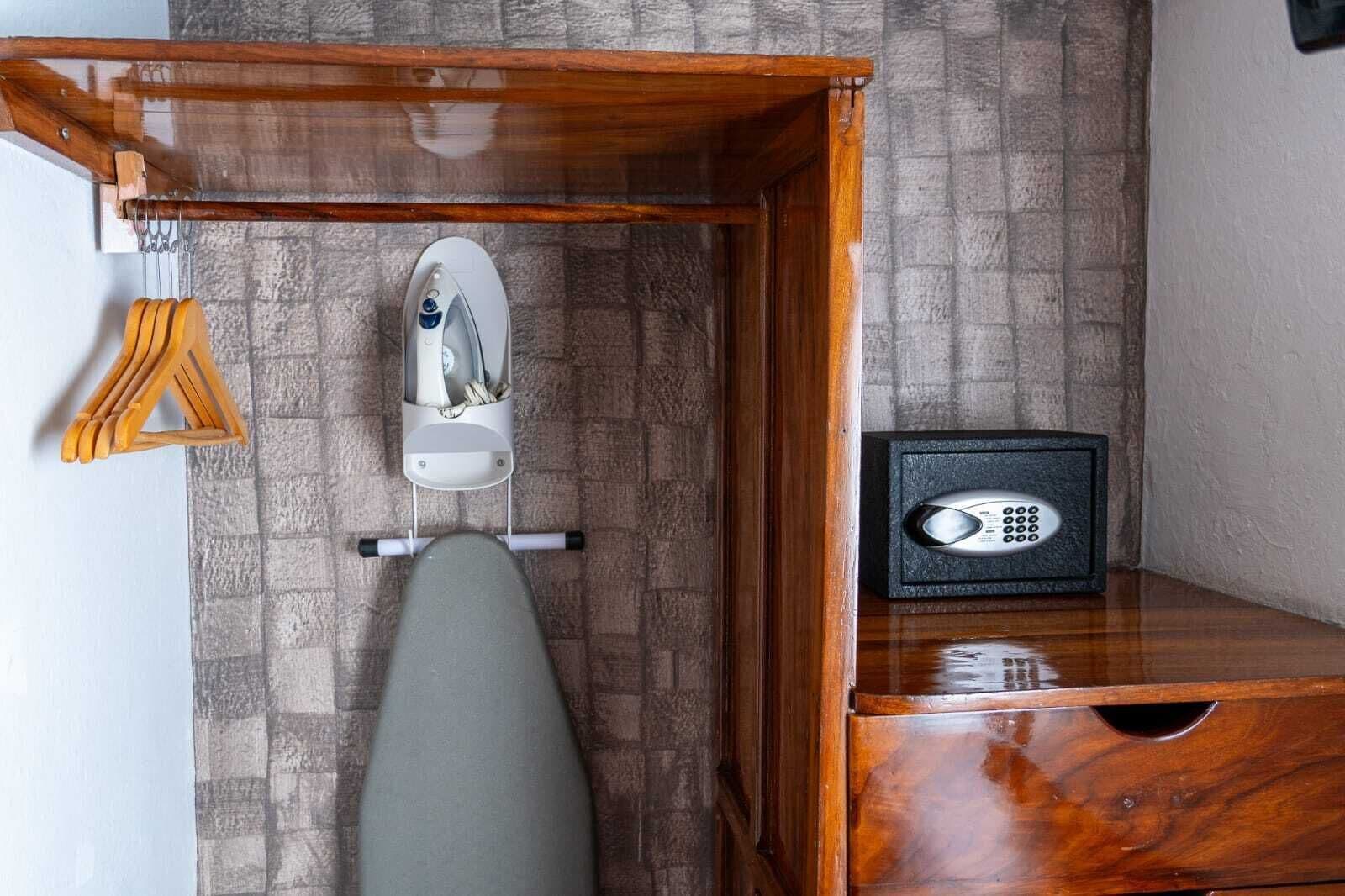 A corner of a room with a wooden ironing board, an iron, and a safe.