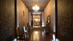 A hallway with a chandelier, wooden chairs, and a cross on the wall. - Hotel Posada del Balsas  (Apatzingan)
