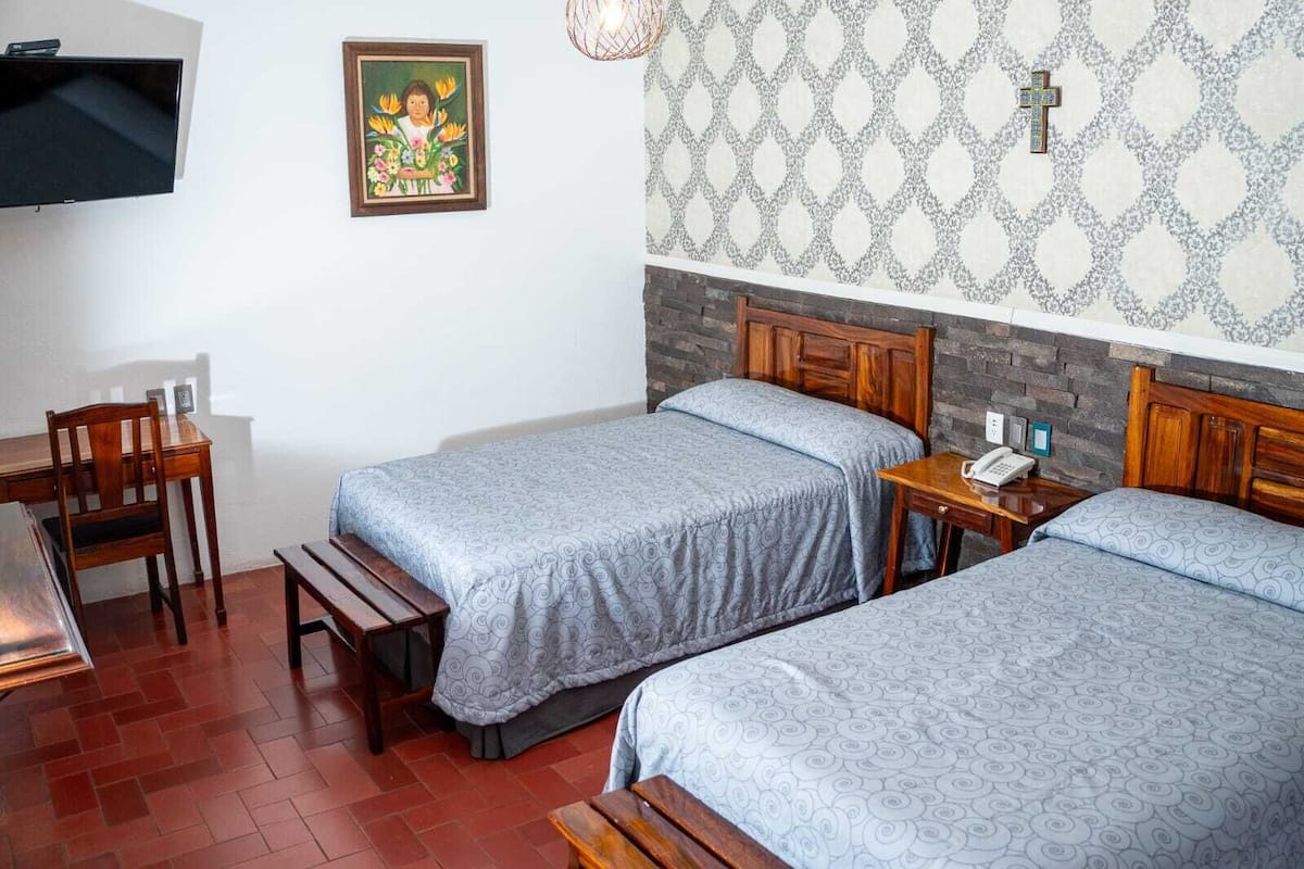 Una habitación con dos camas, un escritorio, una silla, un televisor y un papel tapiz estampado.