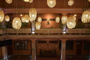 A multi-level hotel lobby with hanging wicker lamps, a central seating area, and decorative wall art.