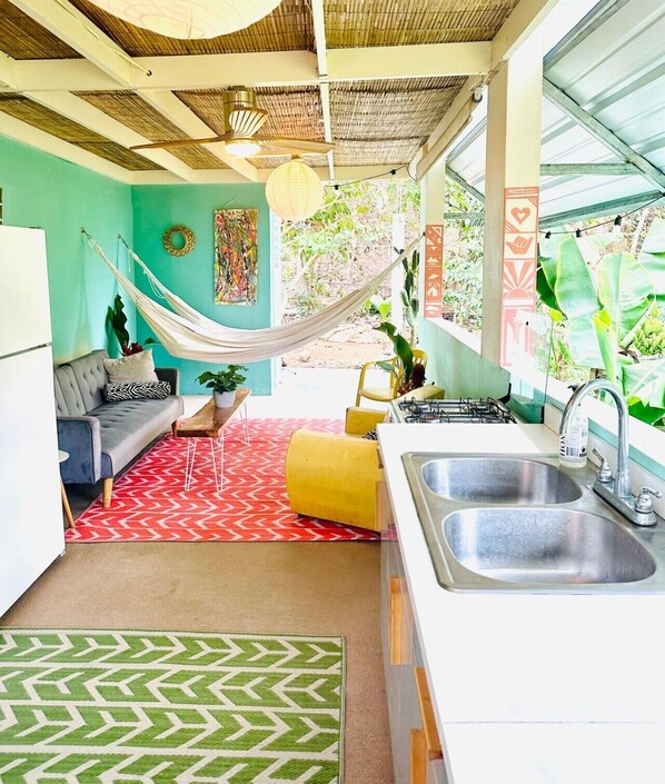 A compact kitchen with a sink, a dining area with a table and chairs, a hammock, and a sofa. - La Casita - Glamping bungalow with AC in Rincón (Rincón)
