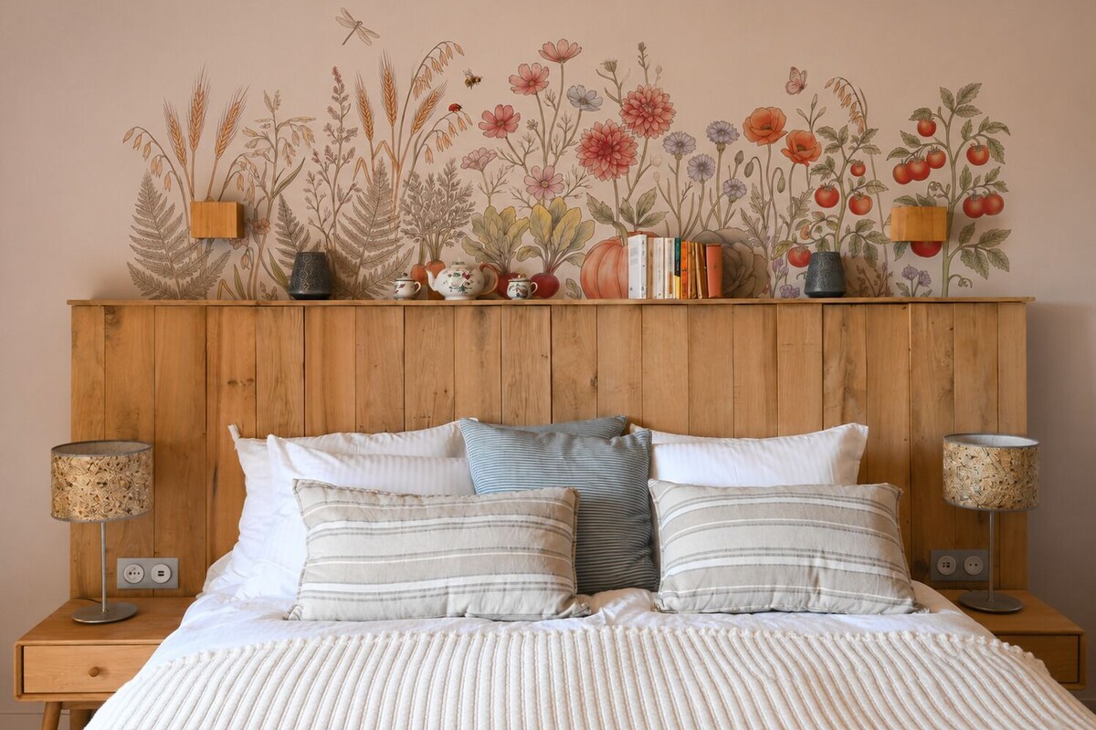 Quarto com cabeceira de madeira, cama com roupa de cama listrada, duas luminárias de cabeceira e um mural floral na parede.
