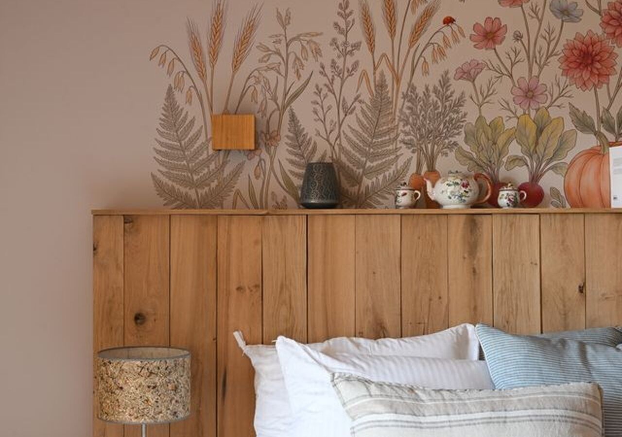 A wooden headboard with a floral wallpaper design, a lamp, and a bed with pillows.