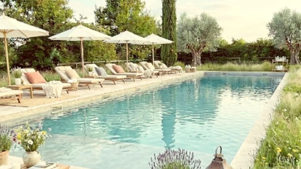 Une piscine entourée de verdure, avec des chaises longues et des parasols.