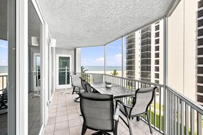 Ein Balkon mit Tisch und Stühlen mit Blick auf einen Strand und ein Hochhaus.