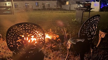 Un'ambientazione esterna notturna con luci a catena, un barbecue e sedie in metallo decorative.