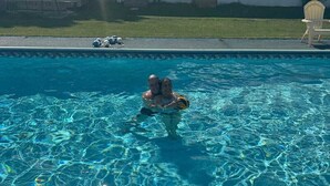 Una piscina con agua cristalina, una silla de descanso y un edificio blanco al fondo.