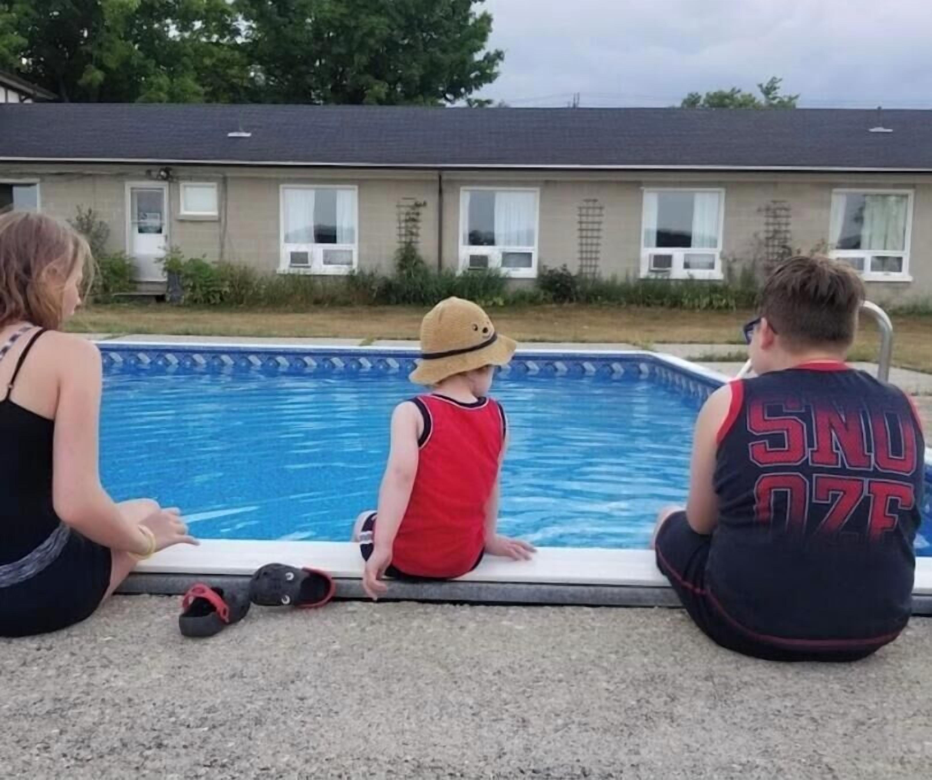 Et boligområde med swimmingpool, et hus i baggrunden og en person siddende ved poolen.