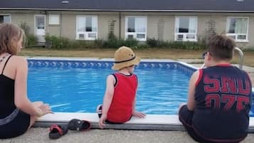 Et boligområde med swimmingpool, et hus i baggrunden og en person siddende ved poolen.
