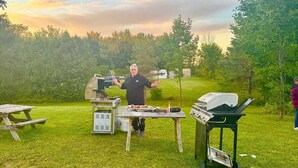Un espacio al aire libre con césped, una parrilla, una mesa de picnic y una estación de asado portátil.