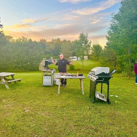 A grassy outdoor area with a barbecue grill, a picnic table, and a portable grill station.. key motel