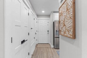 Un couloir avec des portes blanches, un panneau décoratif en bois et un réfrigérateur en acier inoxydable.
