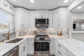 A modern kitchen with white cabinetry, a stainless steel range hood, and a built-in oven. - Sugar Beach F-28 ~ Gulf-side luxury townhome! (Navarre)