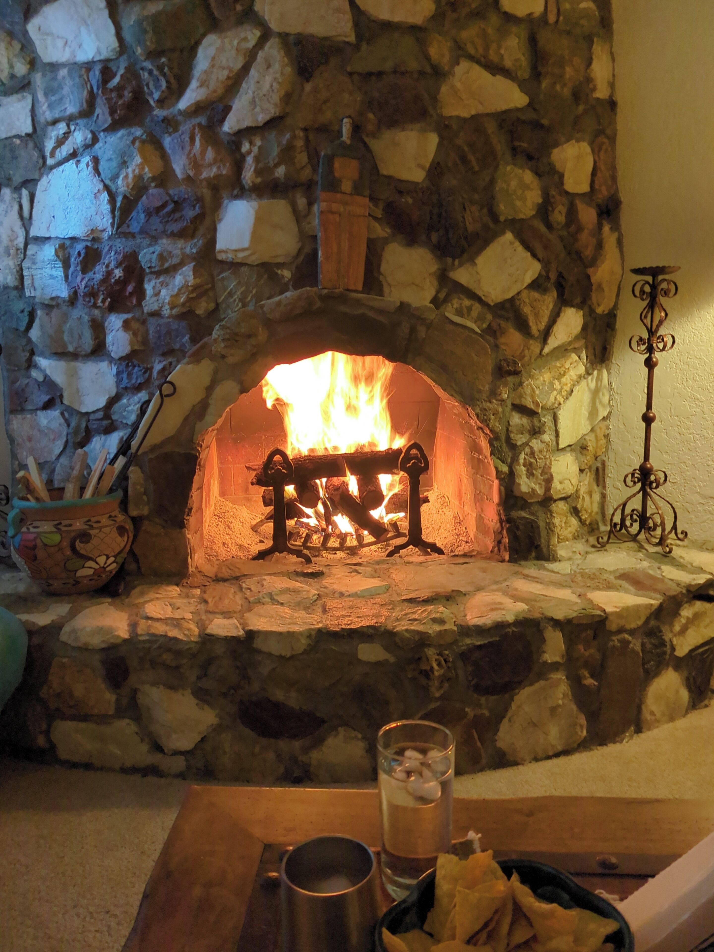 A stone fireplace with a fire, a candle holder, and a glass of water on a table.