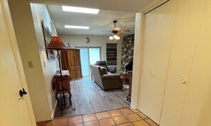 Ein Flur, der in ein Wohnzimmer mit Kamin, Deckenventilator und Tür führt.