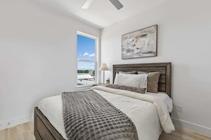 Ein Schlafzimmer mit Bett, Fenster, Lampe und einem Gemälde an der Wand.