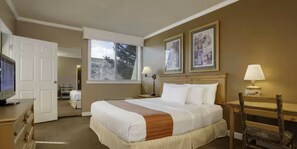 Ein Hotelzimmer mit Bett, Schreibtisch, Stuhl, Fernseher, Fenster und zwei gerahmten Bildern an der Wand.