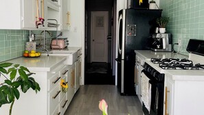 Une cuisine avec des meubles blancs, un réfrigérateur noir, une cuisinière à gaz et un four à micro-ondes.