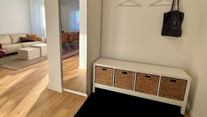 Ein modernes Wohnzimmer mit Sofa, Couchtisch und einem Essbereich im Hintergrund sowie einem Flur, der in ein weiteres Zimmer führt.