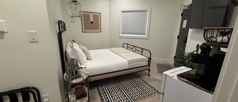 A compact bedroom with a bed, bedside table, and a small desk with a chair.