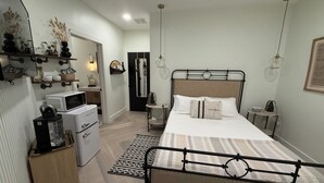 Ein Schlafzimmer mit einem Bett, Nachttischen, einem Schminktisch und einer kleinen Küche mit Mikrowelle und Kühlschrank.