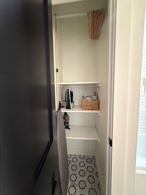 A narrow hallway with a black and white patterned floor, a white door, and a shelf with a basket and a small item.