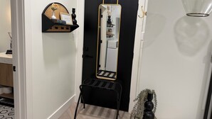 Ein Flur mit einem spiegelnden, schwarz gerahmten Wandbild, einem schwarzen Stuhl und einem kleinen Tisch mit einer Vase.