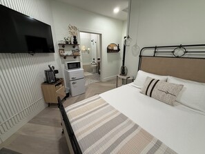 Un dormitorio con cama, mesita de noche y televisor montado en la pared.