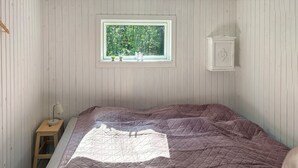 A bedroom with a bed, a window with a view of trees, a small table with a lamp, and a cabinet. - 2 bedroom lovely home in Thyholm (Thyholm)