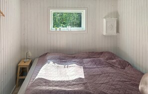Ein Schlafzimmer mit Bett, einem Fenster mit Blick auf Bäume, einem kleinen Tisch mit Lampe und einem Schrank.