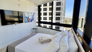 Ein modernes Hotelzimmer mit einem großen Bett, einem Flachbildfernseher und Blick auf die Stadt.