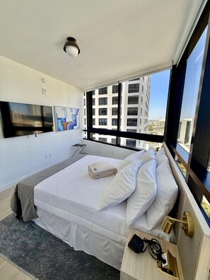 Ein modernes Hotelzimmer mit einem großen Bett, einem Flachbildfernseher und Blick auf die Stadt.