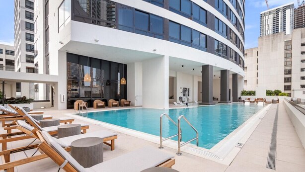 Ein modernes Hotel mit Swimmingpool, Liegestühlen und einer großen Glasfassade.