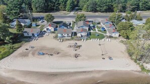 An aerial view of a residential area with numbered houses, a sandy beach, and a road in the background. - 9 cottages on the beach of Lake Huron! (Oscoda)