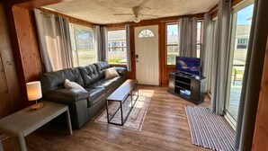 A living room with a leather sofa, a coffee table, a TV on a stand, and large windows with curtains. - 9 cottages on the beach of Lake Huron! (Oscoda)