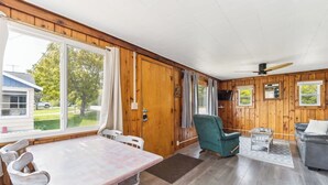 Een vakantiehuisje interieur met een eettafel, stoelen, een bank, een televisie en een plafondventilator.