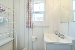 A bathroom with a white sink, a window with a plaid curtain, and a shelf with toiletry items. - #2 | Cozy & Easy - Steps to the Sand (Oscoda)