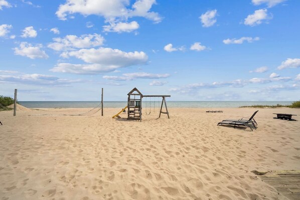 A beach with a lifeguard tower, a swing set, and beach chairs.