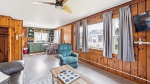 A spacious room with a ceiling fan, a dining area, a kitchen, and a large window. - #2 | Cozy & Easy - Steps to the Sand (Oscoda)