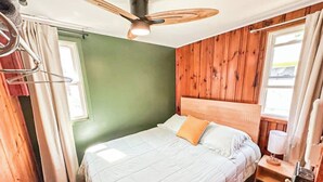 Ein Schlafzimmer mit Bett, Holzwänden, Deckenventilator und Fenster.