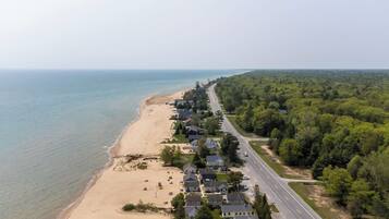 An aerial view of a coastal residential area with houses along the beach, a road, and dense forest.