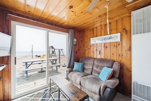 Un interior de madera con sofá, banca, mesa y vista a la playa a través de un ventanal.