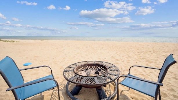 Vista de la playa con una mesa metálica redonda y dos sillas azules.