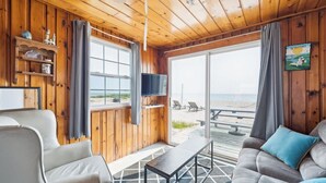 Un interior de madera con televisor, sofá, sillón y vista a la playa.