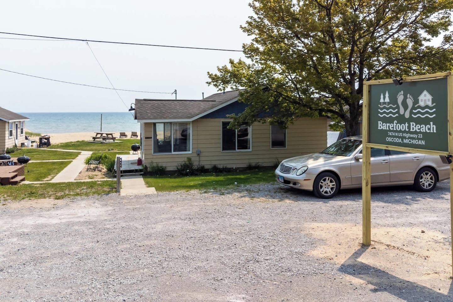 A two-story house with a front yard, a car parked in the driveway, and a sign indicating 'Barefoot Beach' in the background.