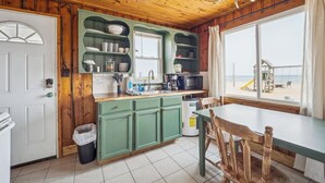 A kitchen with green cabinets, a sink, and a window overlooking a beach.