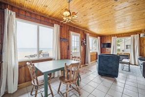 A wooden cabin with a dining table, chairs, a sofa, and a TV. - #5 | Lake Views with Big Windows & New Bath (Oscoda)