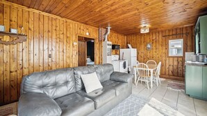 En inredning med träpanel, en soffa klädd i läder, ett matbord med stolar, ett köksområde och ett litet badrum.