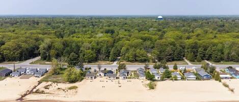 An aerial view of a coastal residential area with houses, a beach, and a water tower in the distance.